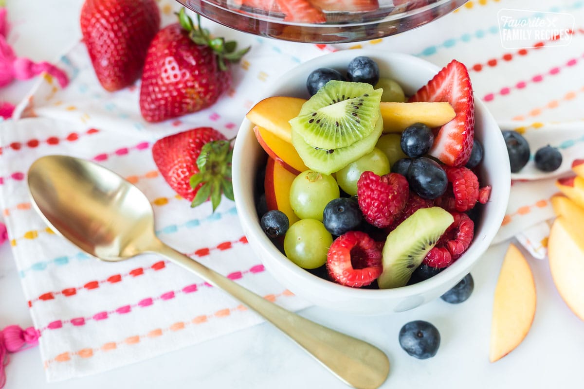 A small bowl of fruit with kiwi, grapes, blueberries, raspberries, strawberries and nectarine slices