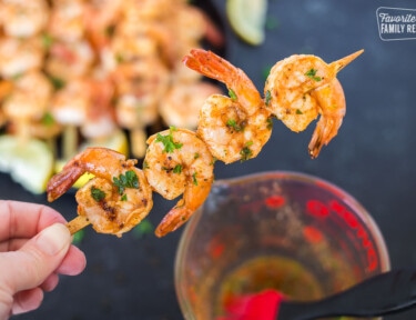 Four cooked shrimp on a skewer next to a bowl of marinade