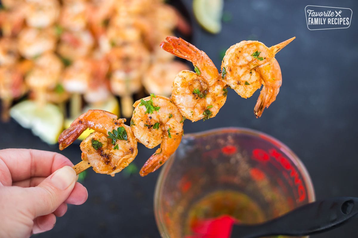 Four cooked shrimp on a skewer next to a bowl of marinade