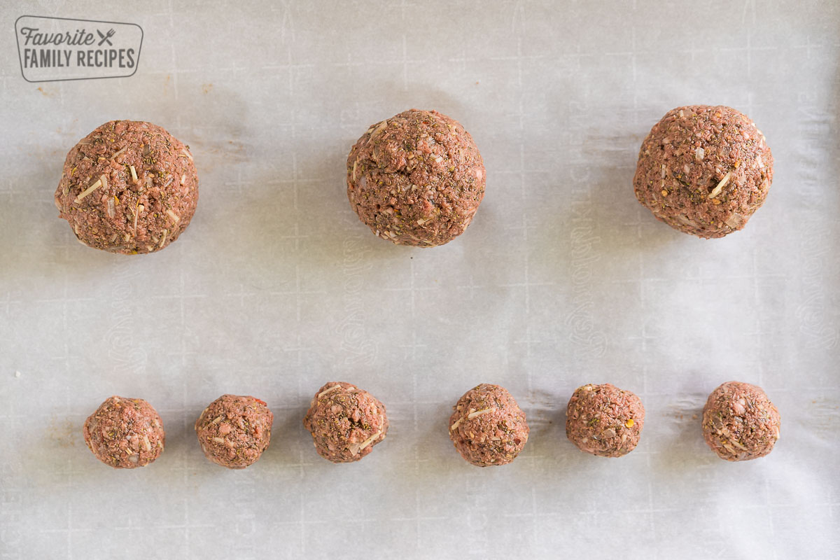 Three large meatballs and six small meatballs on a baking sheet, uncooked