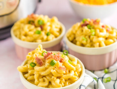 Three pink ramekins full of mac and cheese topped with bacon and green onion