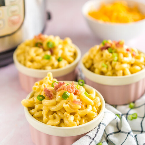 Three pink ramekins full of mac and cheese topped with bacon and green onion