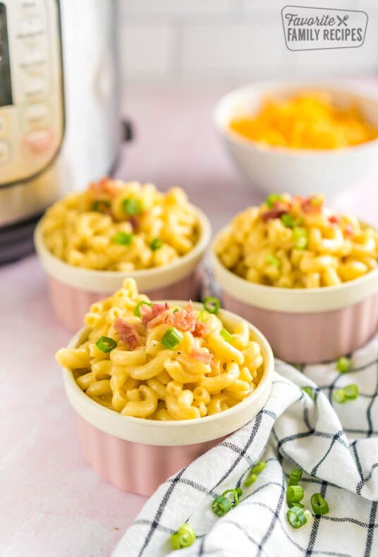 Three pink ramekins full of mac and cheese topped with bacon and green onion