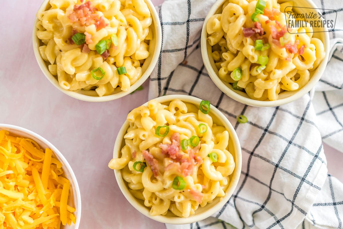 Three pink ramekins full of mac and cheese topped with bacon and green onion.