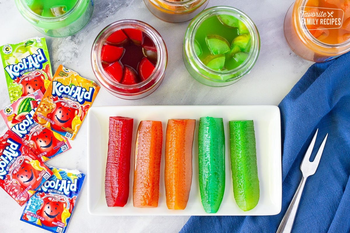 Tired of the same old popular picnic food? Then you should try Kool Aid Pickles! They’re a little sweet, a little tart, and a lot of fun to make and eat. A real adventure for your taste buds! Five colorful spears of Kool Aid Pickles.