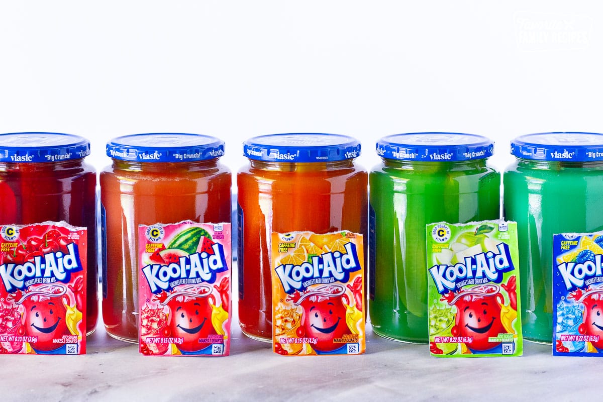 Tired of the same old popular picnic food? Then you should try Kool Aid Pickles! They’re a little sweet, a little tart, and a lot of fun to make and eat. A real adventure for your taste buds! Colorful jars of Kool Aid Pickles.