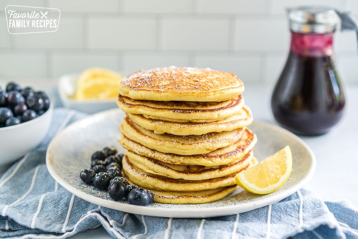 A stack of lemon ricotta pancakes on a plate with blueberries and a lemon wedge.