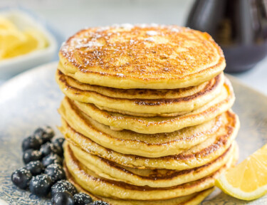 A stack of lemon ricotta pancakes on a plate with blueberries and a lemon wedge