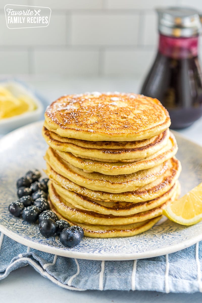 A stack of lemon ricotta pancakes on a plate with blueberries and a lemon wedge.