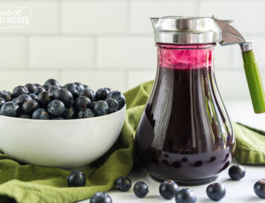 Blueberry syrup in a dispenser next to a bowl of blueberries