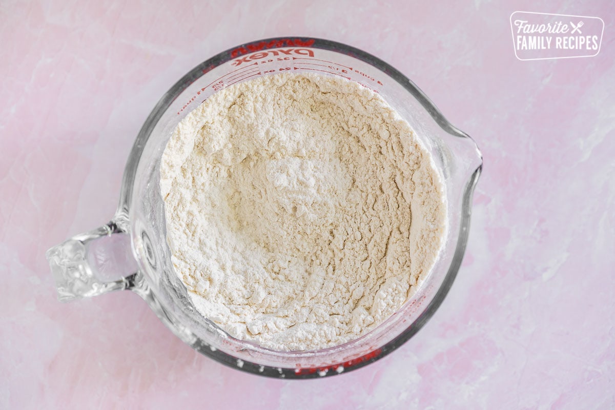 A measuring cup full of flour, baking soda, baking powder, and salt