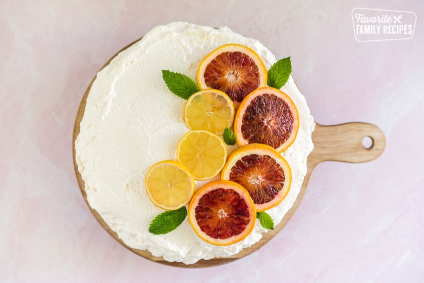 Olive oil cake decorated with whipped cream, blood orange slices, lemon slices, and mint leaves