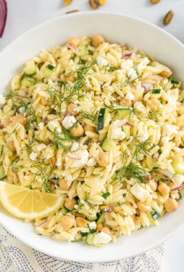 A large white bowl full of orzo salad garnished with fresh dill and a lemon wedge