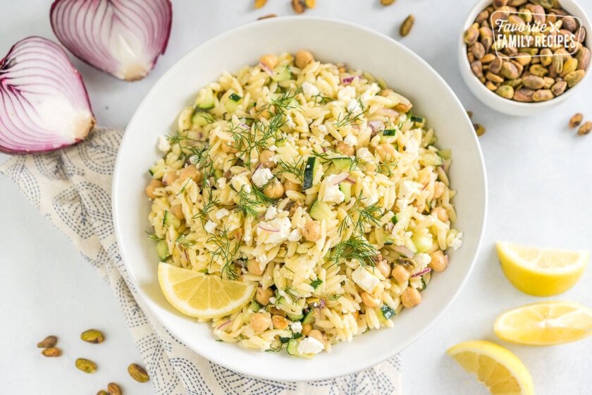 A large white bowl full of orzo salad garnished with fresh dill and a lemon wedge
