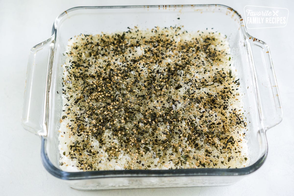Rice pressed into the bottom of the baking dish with furikake seasoning sprinkled on top