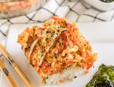 A scoop of sushi bake on a plate with seaweed snacks and chopsticks