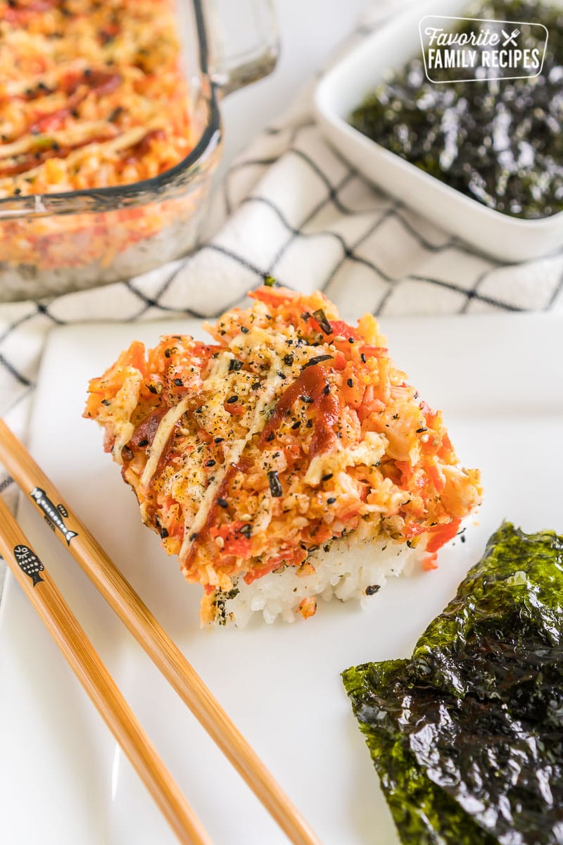 A scoop of sushi bake on a plate with seaweed snacks and chopsticks