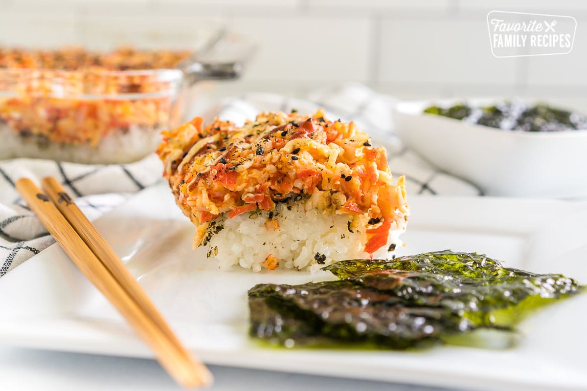 A scoop of sushi bake on a plate with seaweed snacks and chopsticks