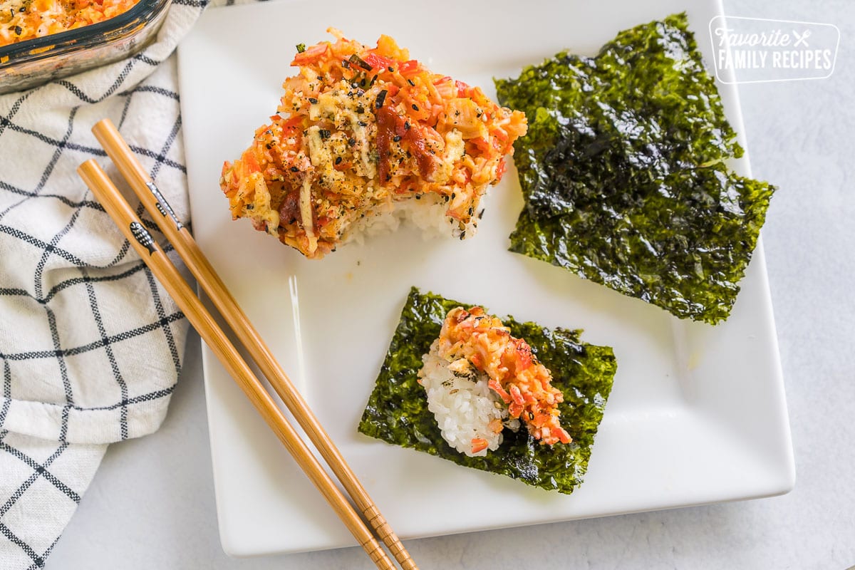 A scoop of sushi bake on a plate with seaweed snacks and chopsticks