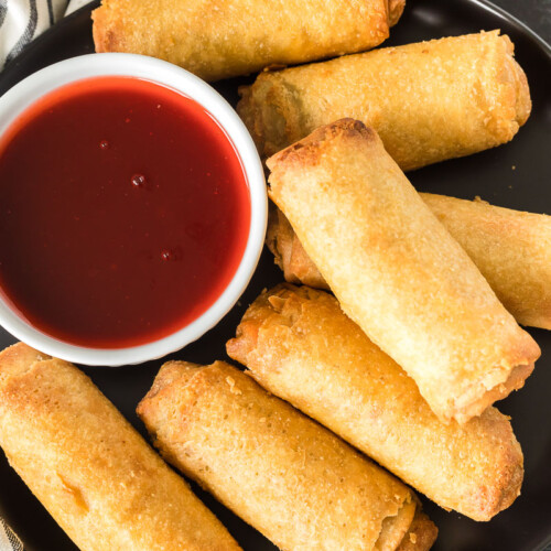 Egg rolls on a plate with a bowl of sweet and sour sauce