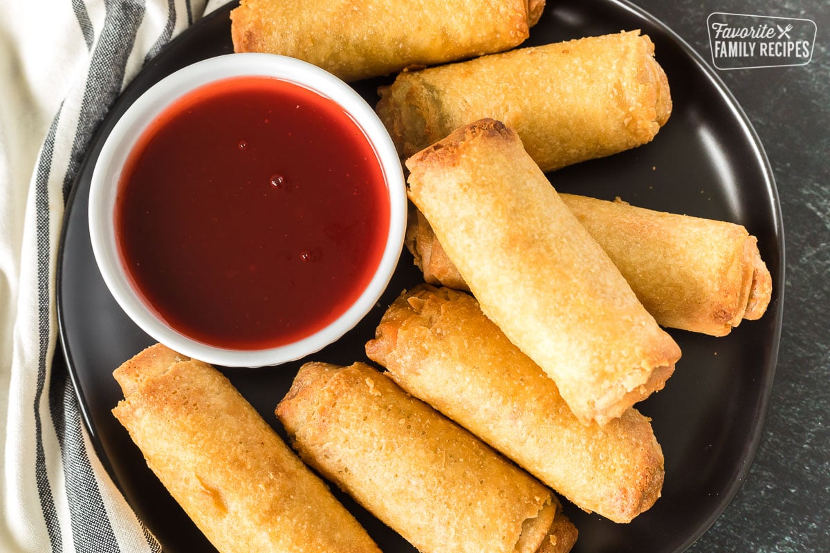 Egg rolls on a plate with a bowl of sweet and sour sauce.