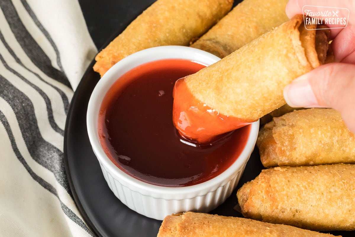 A fried egg roll being dipped in sweet and sour sauce.