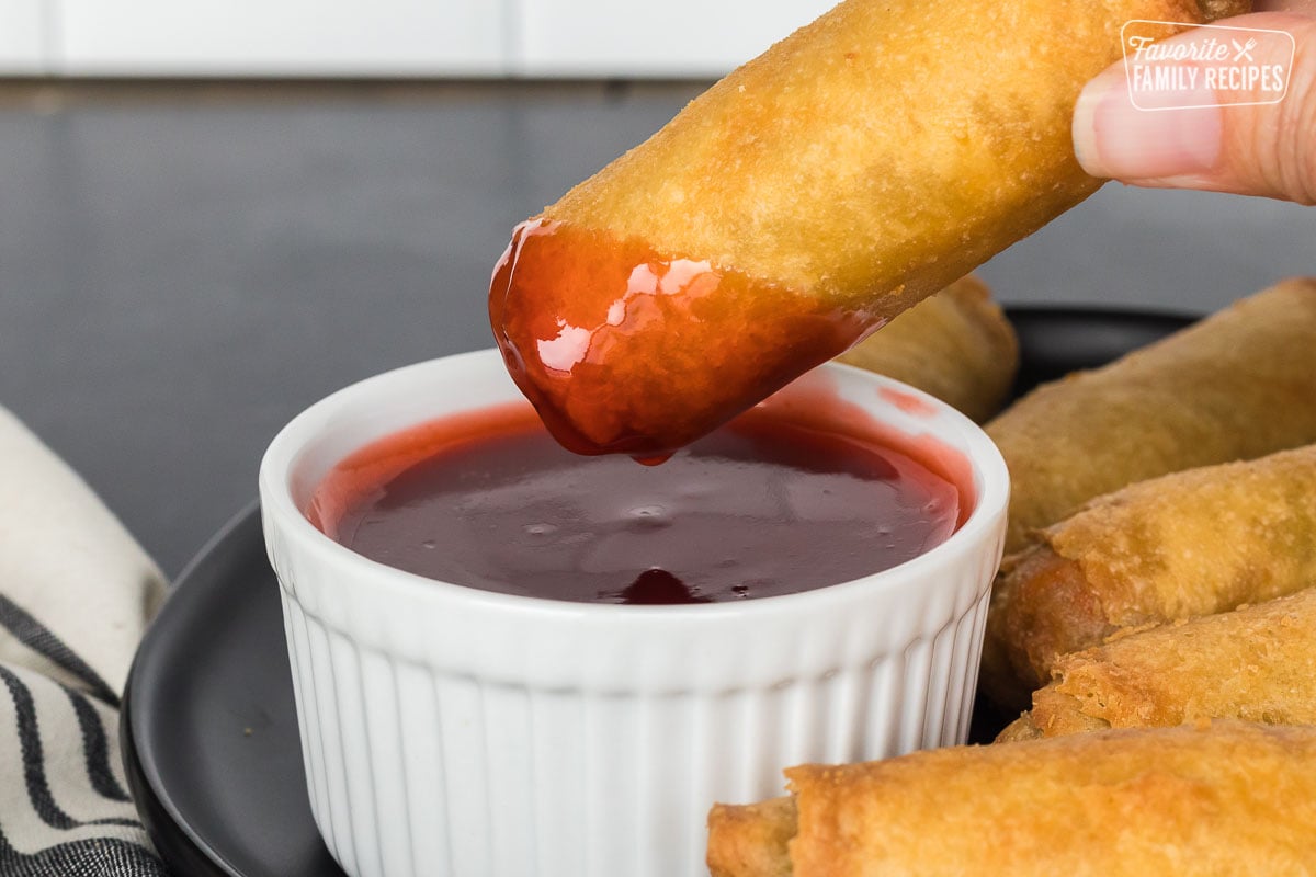 A fried egg roll being dipped in sweet and sour sauce.