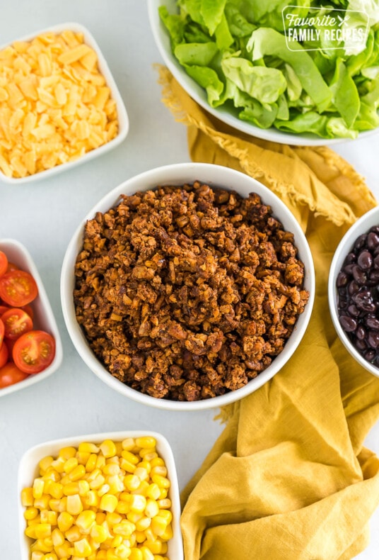 Vegan taco meat in a bowl surrounded by bowls of taco toppings