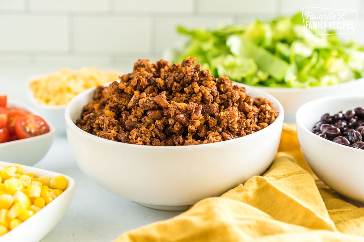 Vegan taco meat in a bowl surrounded by bowls of taco toppings.