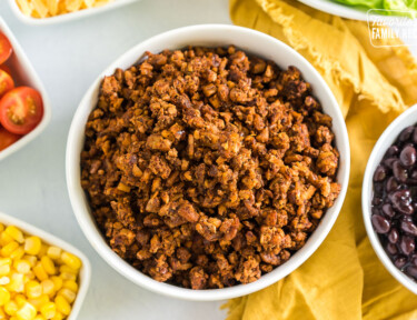 Vegan taco meat in a bowl surrounded by bowls of taco toppings