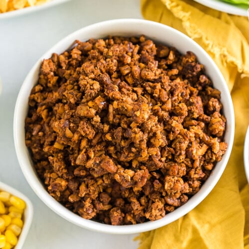 Vegan taco meat in a bowl surrounded by bowls of taco toppings