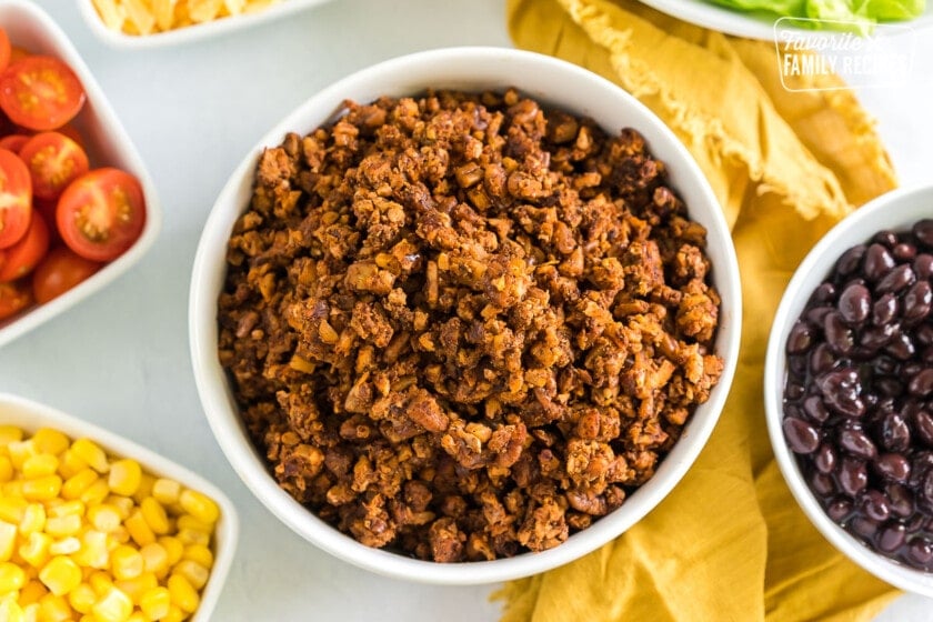 Vegan taco meat in a bowl surrounded by bowls of taco toppings