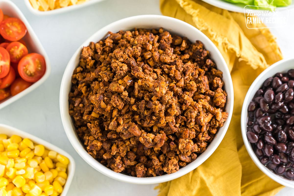 Vegan taco meat in a bowl surrounded by bowls of taco toppings.