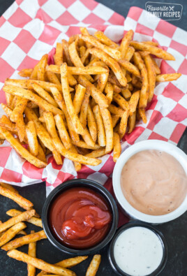 Cooked French fries in a basket next to three dipping sauces