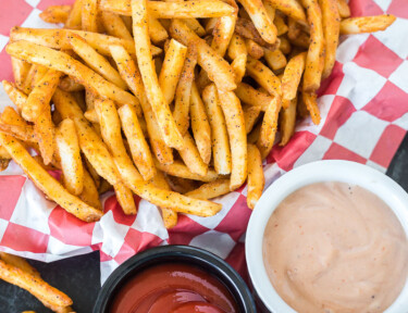 Cooked French fries in a basket next to three dipping sauces