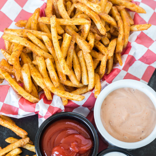 Cooked French fries in a basket next to three dipping sauces