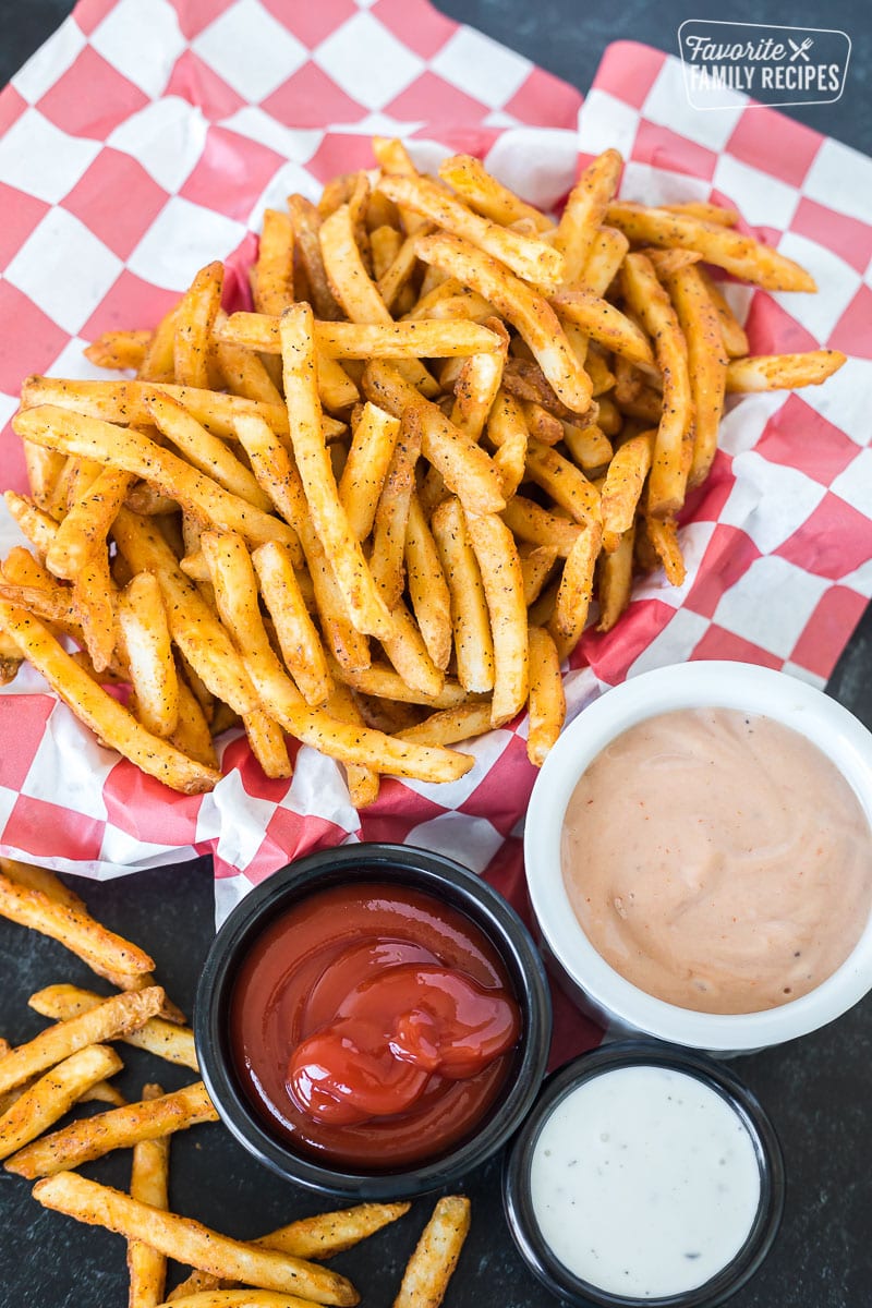 Cooked French fries in a basket next to three dipping sauces