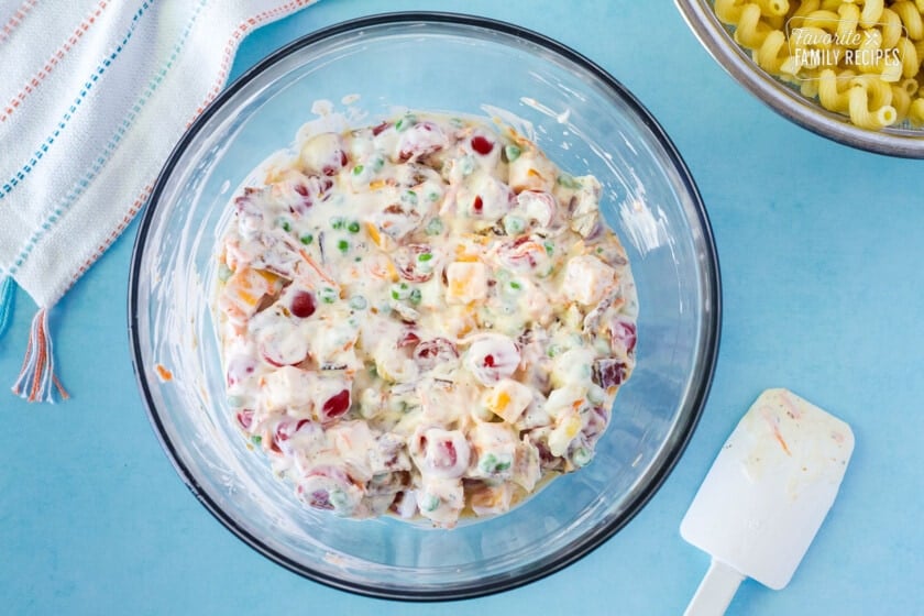 Bowl with creamy salad mixture of tomatoes, cheddar cubes, peas, carrots and bacon.