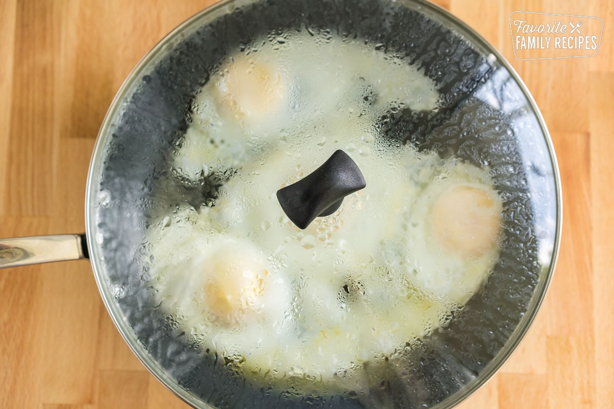 A covered skillet containing four eggs