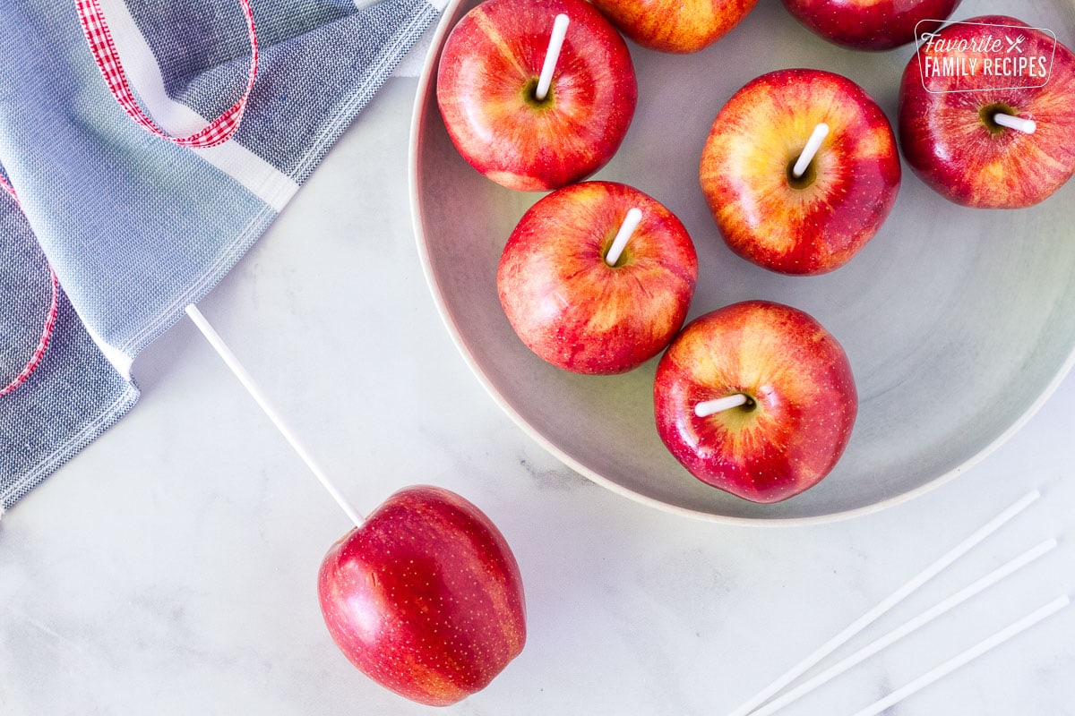 Plate of fresh apples with candy sticks pushed in the middle.