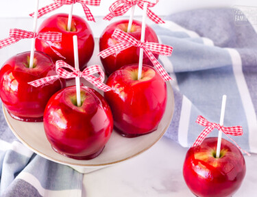 Five Candy Apples on a cake stand with one on the table.