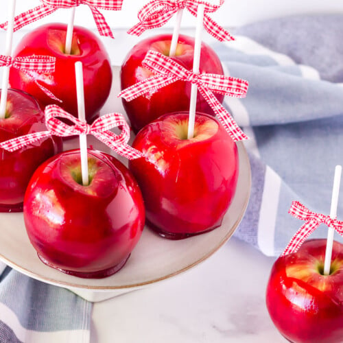 Five Candy Apples on a cake stand with one on the table.