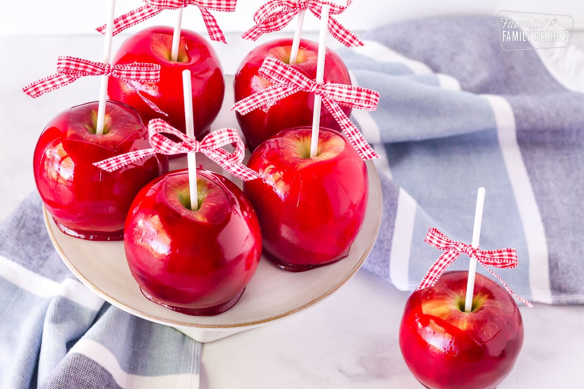 Five Candy Apples on a cake stand with one on the table.