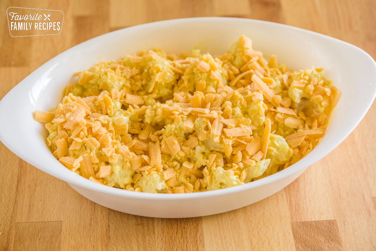 Cauliflower florets coated with sauce and topped with shredded cheese in an oval baking dish
