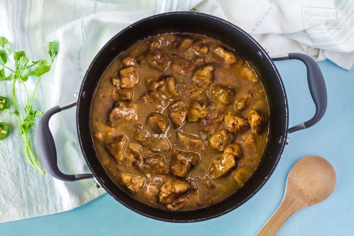 Green enchilada sauce and seasonings added to pot of simmering Pork Chili Verde with a wooden spoon on the side.