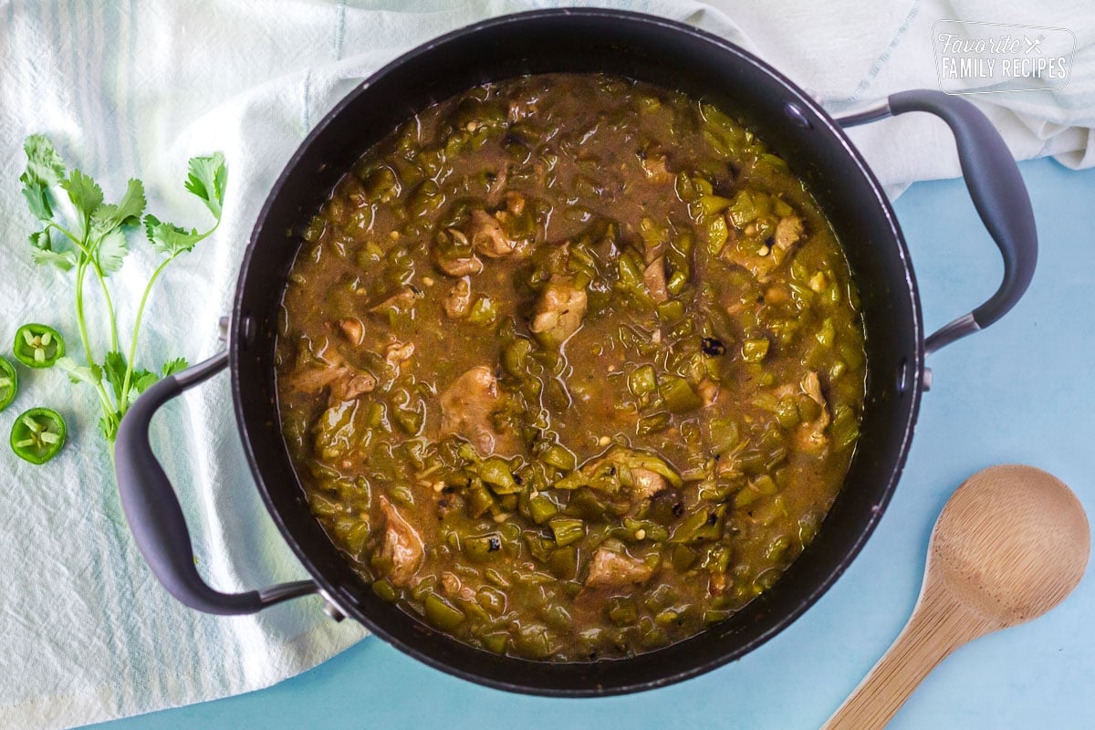 Green Chiles added to pot of simmering Pork Chili Verde. Wooden spoon on the side.