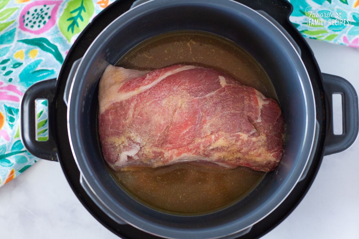 Liquids around a raw pork roast in a slow cooker to make Kalua Pork.