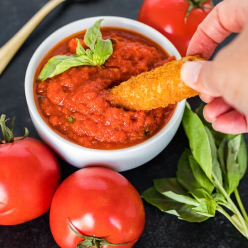 A mozzarella stick being dipped in marinara sauce