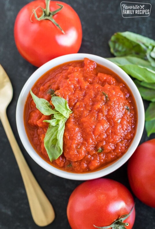 A small bowl with marinara dipping sauce next to fresh tomatoes