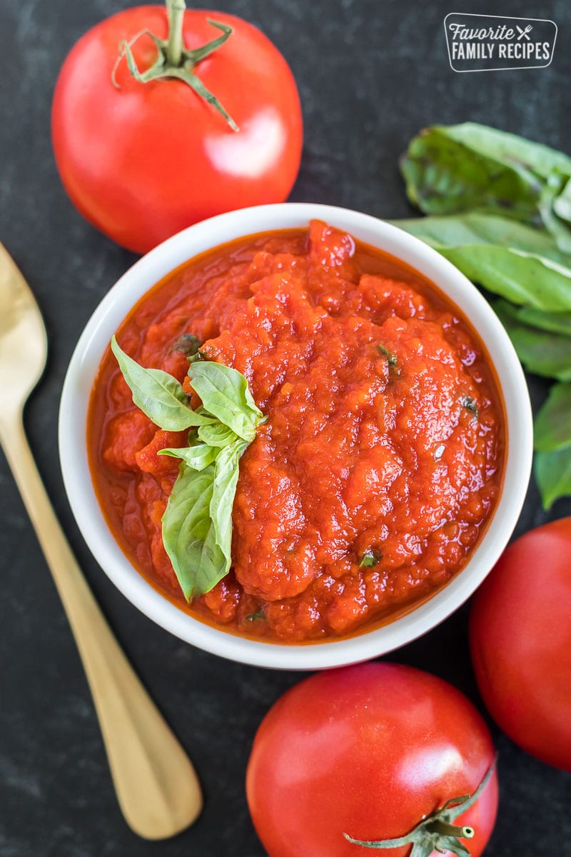 A small bowl with marinara dipping sauce next to fresh tomatoes